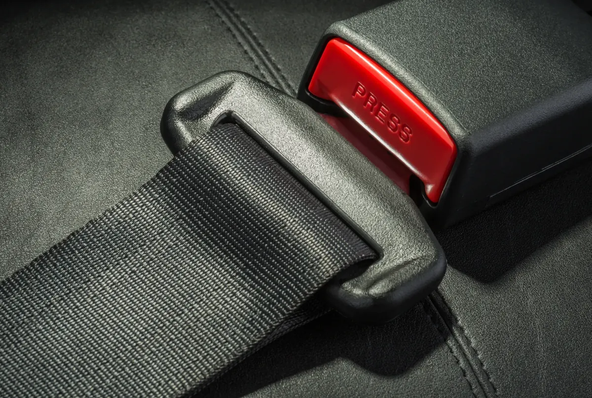 Close-up of seat belt webbing, latch plate and buckle receiver on a dark leather seat