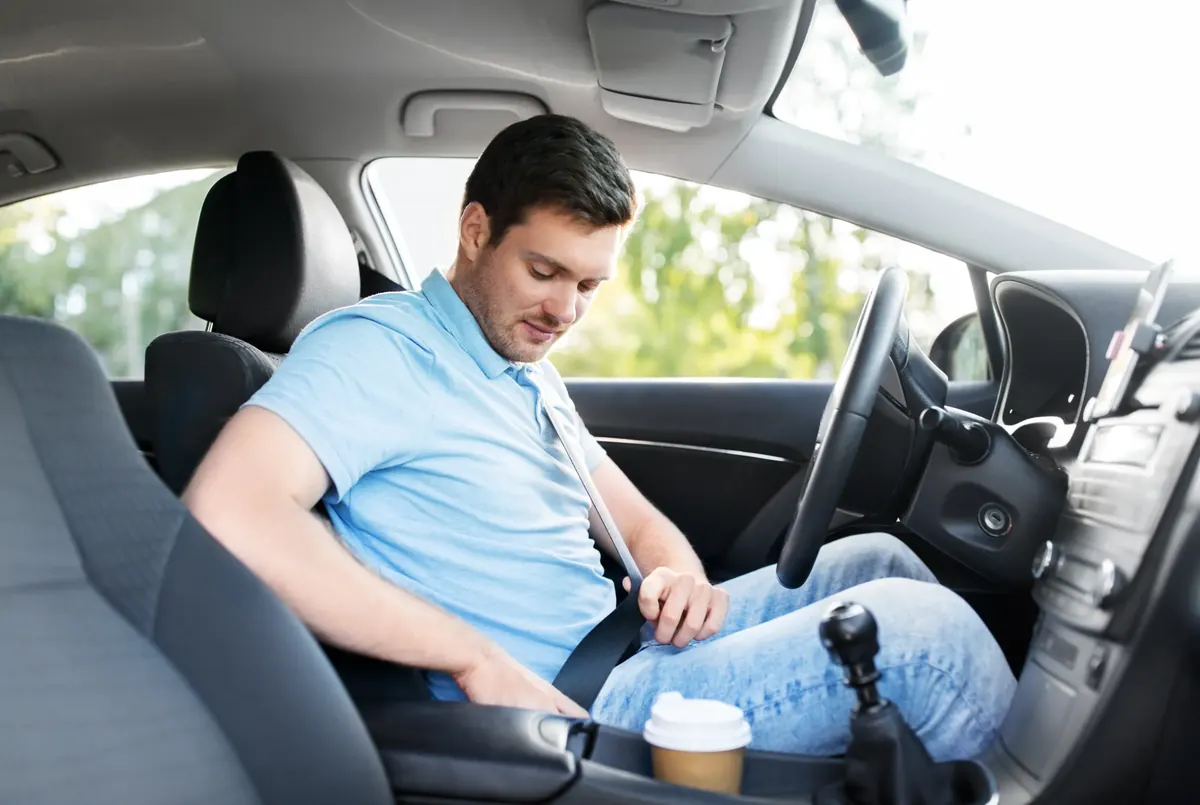 Driver in a passenger car reaching down to fasten the seat belt beside the seat