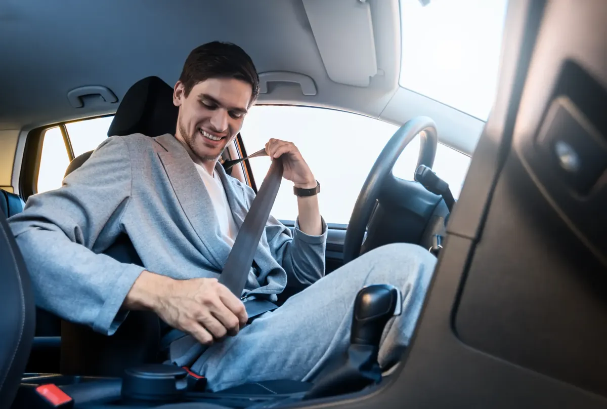 Driver seated in a car drawing the seat belt across the body to fasten it