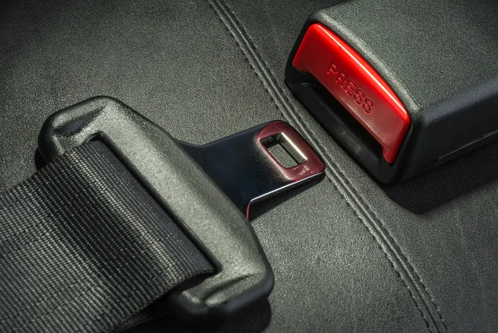 Close-up of seat belt webbing and latch plate resting on a dark seat surface