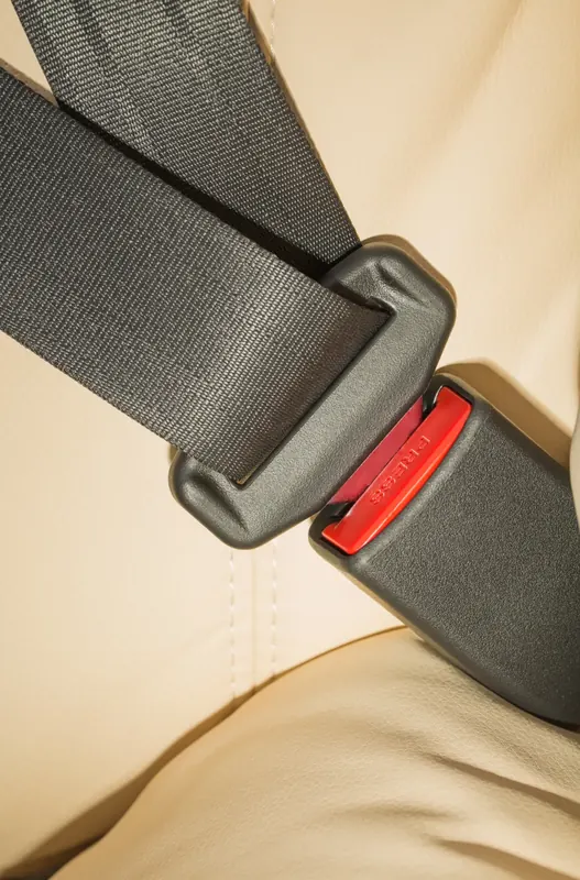 Seat belt webbing entering a buckle on a light leather seat