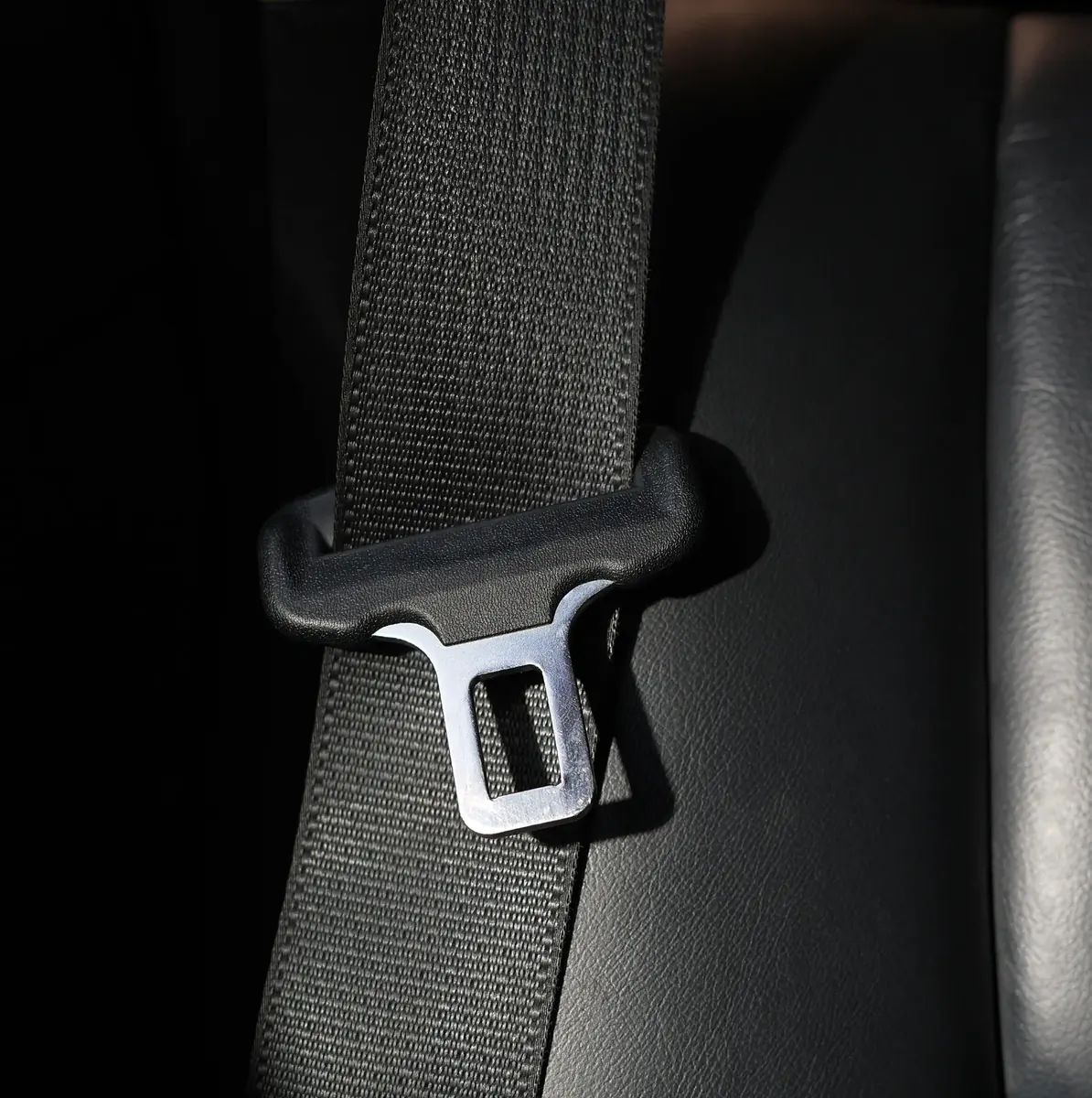 Seat belt webbing running through a guide with a metal latch plate against a dark interior