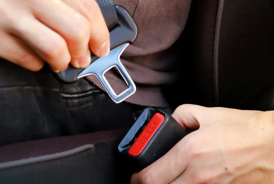 Two hands bringing a seat belt latch plate and buckle together between vehicle seats