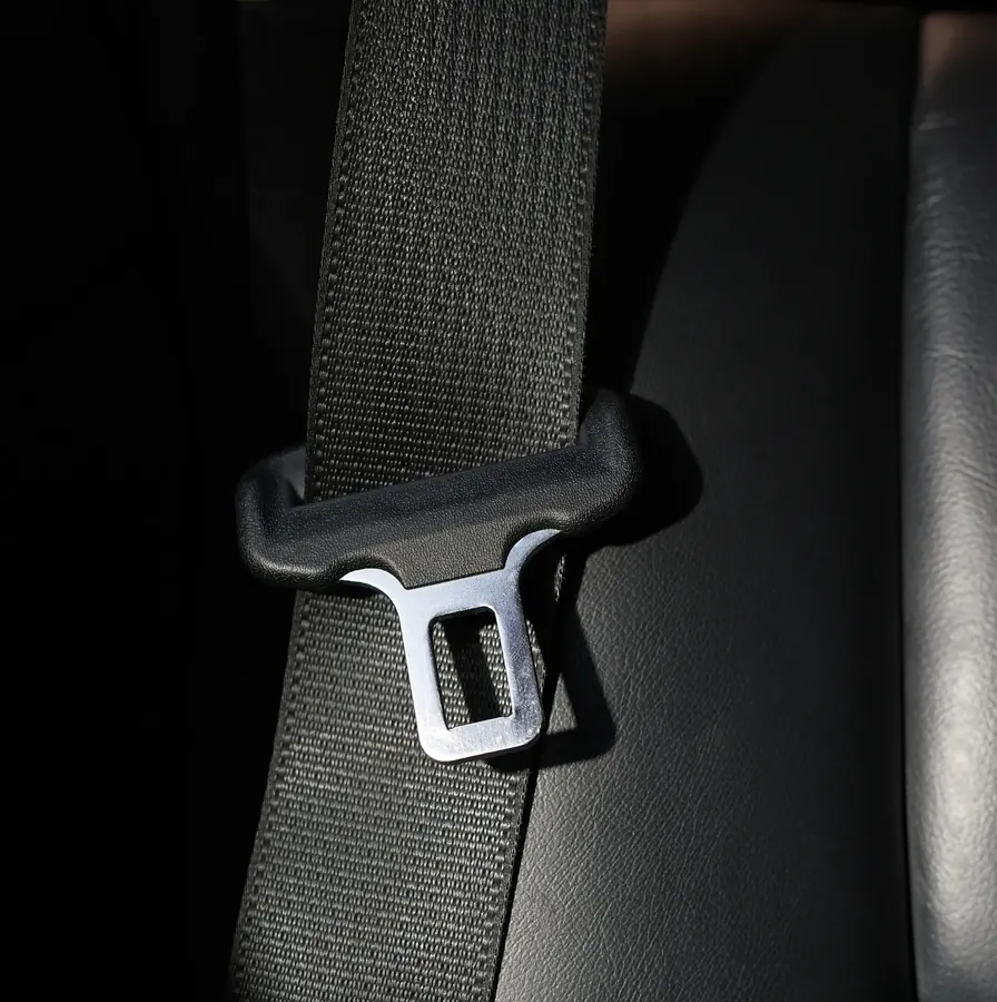 Seat belt webbing running through a shoulder guide with a polished metal latch plate