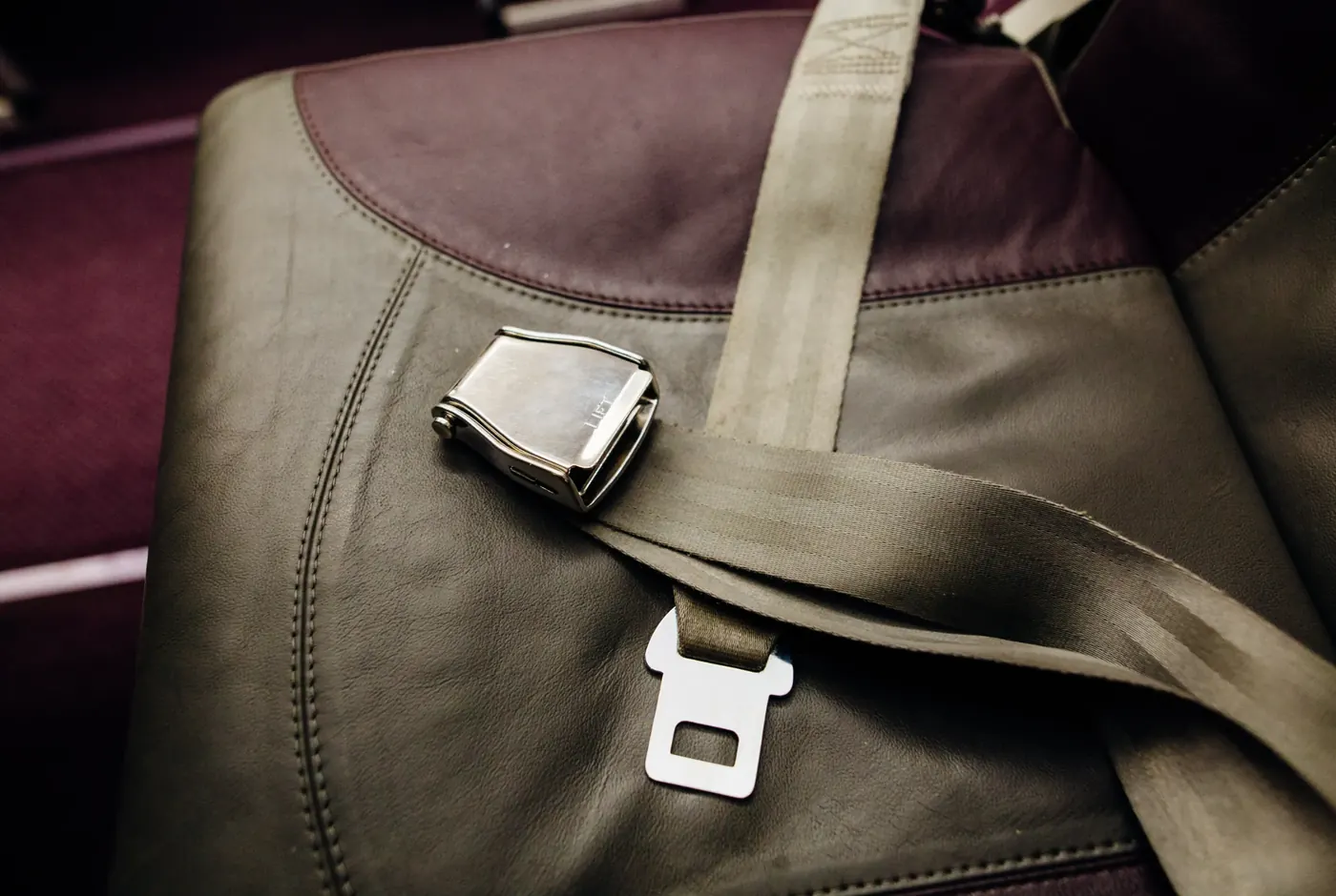 Metal lift-latch lap belt buckle and webbing resting on an olive upholstered seat