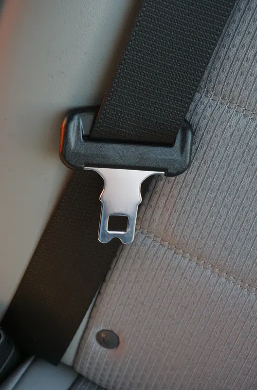 Metal seat belt latch plate resting against webbing on a grey vehicle seat
